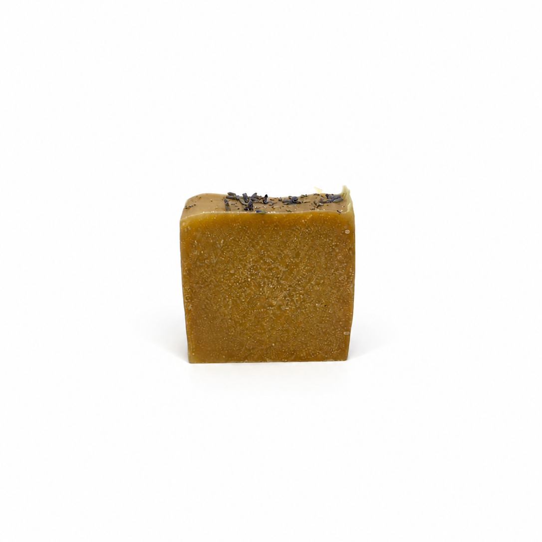 Brown square of soap topped with dried lavender on white background.