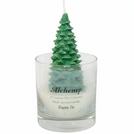 Green Christmas tree-shaped candle in a glass holder with 'Alchemy' branding on a white background